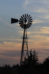 windmill at sunset with a colorful sky with white clouds out in the country west of Nickerson Kansas USA.