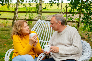 Senior man and female sitting in armchairs and drink a tea in garden