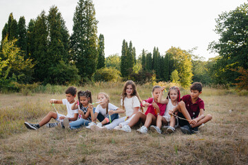 A large group of cheerful children sit on the grass in the Park and smile. Games in a children's...