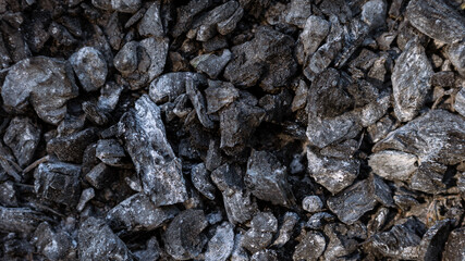 Scattered pieces of embers in hearth mixed with ash. Black charcoal briquettes