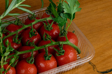 ripe red tomatoes in transparent container with herbs, close-up photo, space for text on wooden background.