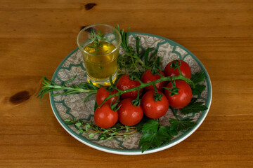 cherry tomatoes on wooden table over white plate with olive oil with herbs. light background, close-up photo