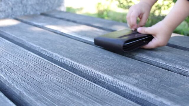 The lost wallet on the park bench is taken by the child's hand. Lost item on the street