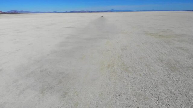 Back view from drone of horsepower automotive red transport driving in desolate dry basin practicing extreme drifting and bashing for feeling adrenaline from high auto speed riding
