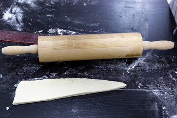 The dough is in the shape of a triangle next to a rolling pin as a croissant blank.