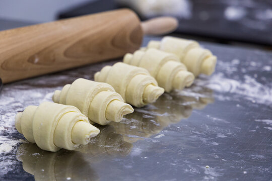 Raw shaped croissants next to a rolling pin on a table with flour. The handmade croissant preparation process