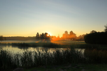 Misty landscape in the early morning at a golf course. Sun risning the east. Next to a small lake....