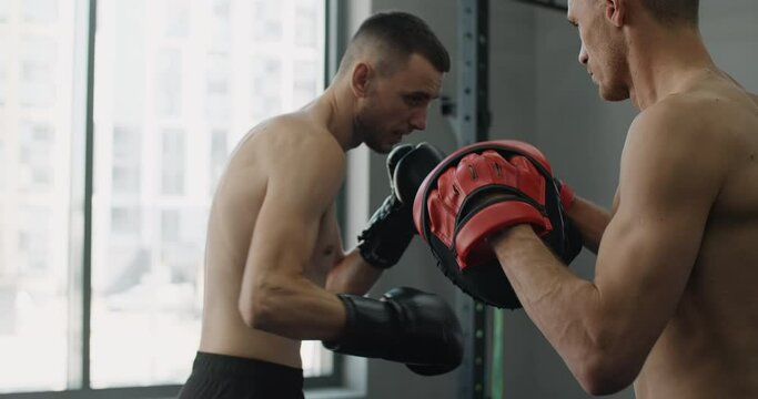 Fighter in boxer gloves is practising his strikes with trainer in slow motion in the gym, kickboxers are training, 4k 120fps Prores HQ