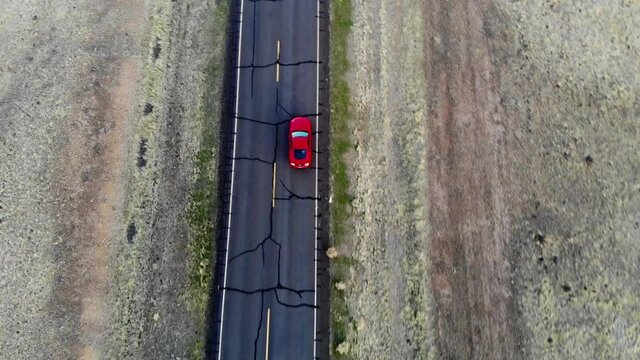 Aerial bird's eye of red car doing automotive riding during getaway trip in wild lands with asphalt freeway, overhead of speed powerful automobile driving
