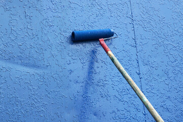 A paint roller on a long handle applies new blue paint to the old one. Construction and renovation...