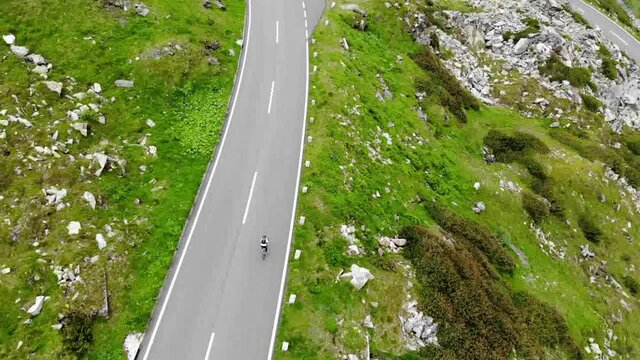 Bird's eye aerial of active wheelman ride on transport bike on serpentine hairpins roadway, drone above view of male cycler on bicycle exploring world during getaway travel for recreation
