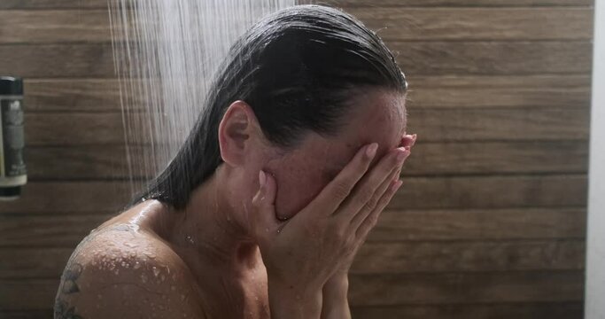 Desperate young woman hiding face with hands and crying while taking shower in bathroom