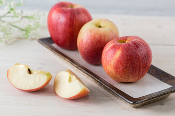 In a rectangular dish on white wooden table are three juicy beautiful ripe red apples of the early winter variety Gala. Next to the slices of the cut fruit