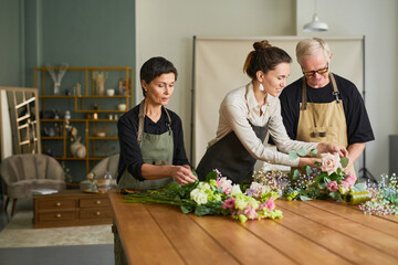 Waist up portrait of young female florist teaching mature couple arranging flower compositions in...