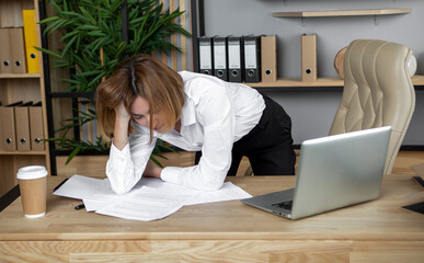 Attractive female business woman working in bending over the desktop full of paper work. She is nervous and tired