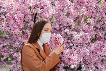 A young girl takes off her mask and breathes deeply after the end of the pandemic on a Sunny spring day, in front of blooming gardens. Protection and prevention covid 19