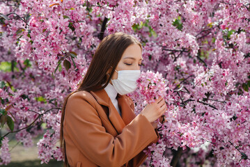 Fototapeta premium A young girl takes off her mask and breathes deeply after the end of the pandemic on a Sunny spring day, in front of blooming gardens. Protection and prevention covid 19