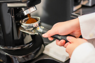 Close-up shot of freshly ground coffee being poured into a grinder by a barista in a cafe