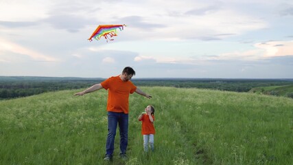 Family prazniki outdoors. Child and dad play together with kites in front of the sky in the park. Happy family, daughter and dad raise a kite into the sky. The concept of healthy children and parents.