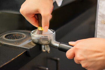Woman making coffee in a cafe holding portafilter with pressed ground coffee inside it