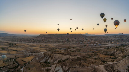 Cappadocia, Turkey: Wide angle Panorama aerial shot of colorful hot air balloons together floating in the sky at early morning in Goreme against volcanic hills