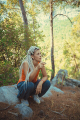 a Rastafarian girl with dreadlocks sits and smokes on a stone