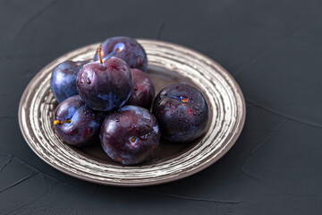 ripe plums on a brown plate, black textured background, selective focus