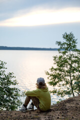 little girl sits on the shore of the lake and looks at the sunset. back view