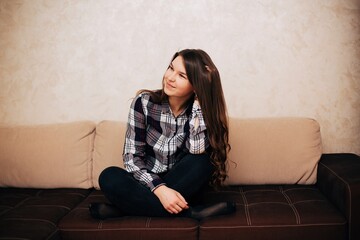 Girl in a cardigan shirt sitting on the couch. Long haired brunette sitting on the couch at home