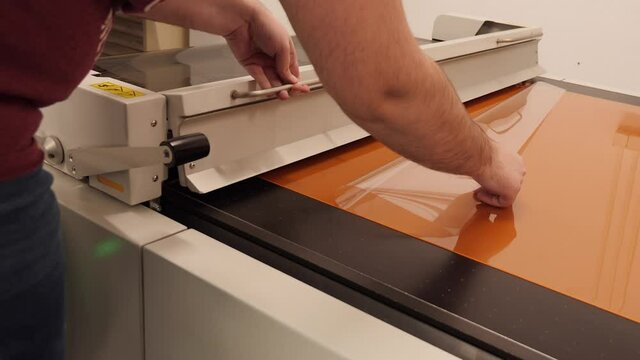 Worker hands operate digital flexographic machine - laminating the thermal imaging film on the carrier plates