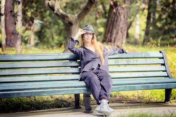 Fototapeta premium A woman in lilac clothes and a hat sits on a park bench on a sunny day