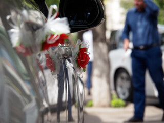 Artificial flower on the handle of a wedding car against the backdrop of a man in blue clothes. Same-sex marriage as a trend in modern society or as an exception in traditional society.
