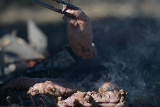 Metal clamp grabbing chinchulines and molleja, cooked on the coals in a grill.