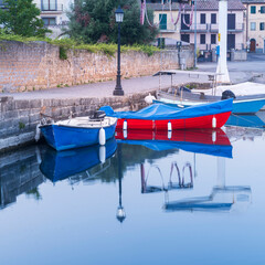 Fototapeta na wymiar two boats and street lighter with reflections in water in city Capodimonte in Lazio in Italy