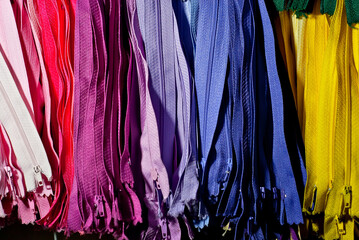 Multicolored zipper locks in a clothing store. Many colored strips of fabric hang on the wall....
