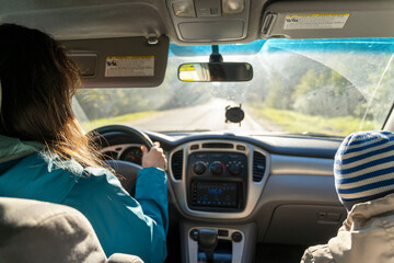 a woman driving a car with a child in the passenger seat, a young woman driving her car, an inside view