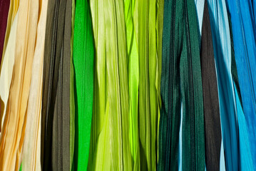 Multicolored zipper locks in a clothing store. Many colored strips of fabric hang on the wall....