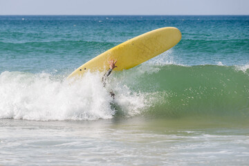 Surfer dangerously falls of his yellow soft top surfboard.
