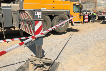 Outriggers of heavy all-terrain mobile crane at construction site. Crane work execution area fenced with a signal tape. Exclusion dropped zone