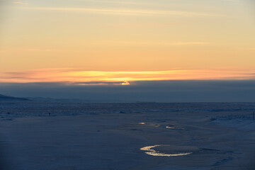 Arctic landscape in winter time. Small river with ice in tundra. Sunset.