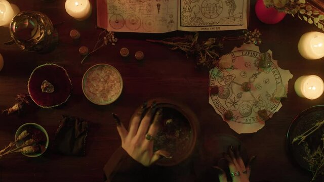 Witch cooking potion elixir top view. Table with spellbook for making rite. Herbs, burning candles, crystal magic ball for sacrifice. Halloween theme, full moon, witchcraft. 