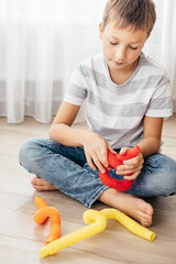 Colorful anti-stress fidget push pop tube toys for children. Flexible corrugated pipe in kids hands. Boy playing with sensory toys. Fun playing for developing imagination and fine motor skills. - obrazy, fototapety, plakaty