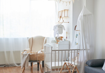 Scandinavian style white interior  bedroom, nursery. Baby cot with ​canopy. Wooden shelves and toys. Armchair in children's room