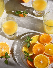 Glasses of fresh orange juice and orange slices with mint leaves on a white background