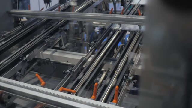 White cardboard sheet moving fast on conveyor line of automatic carton box making machine at food package exhibition, trade show. Industrial, equipment, technology concept