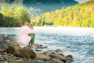 The woman alone covered her head with her hands and cries in the open air. Stormy river, mountains on the background.