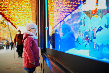 Obraz na płótnie Canvas Toddler girl looking at window glass of large department store decorated for Christmas