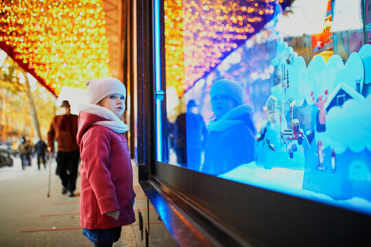 Toddler girl looking at window glass of large department store decorated for Christmas