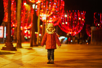 Adorable preschooler girl on Champs Elysees with its traditional Christmas illumination in Paris,...