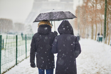Couple passing by the Eiffel tower in Paris on a day with heavy snow - obrazy, fototapety, plakaty
